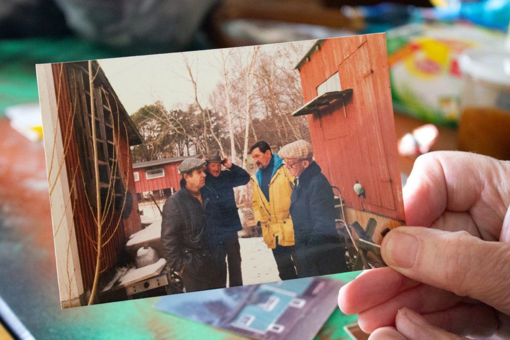 Lasses hand håller i ett gammal fotografi på fyra män som står och pratar med varandra. Det är vinter och tre av dem har basker på sig.