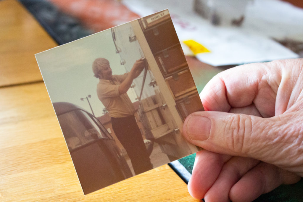 Lasse håller i ett gammalt fotografi på sig själv. På fotografiet håler Lasse på att öppna lastbilen där duvorna finns.