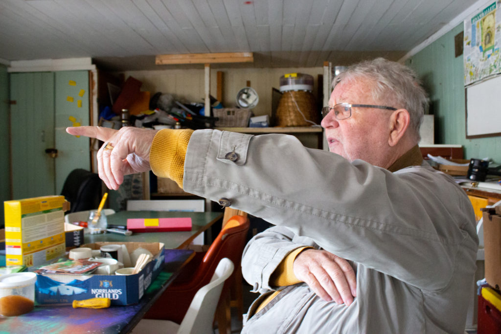 På bilden sitter Lasse på en stol och pekar mot ett fönster.