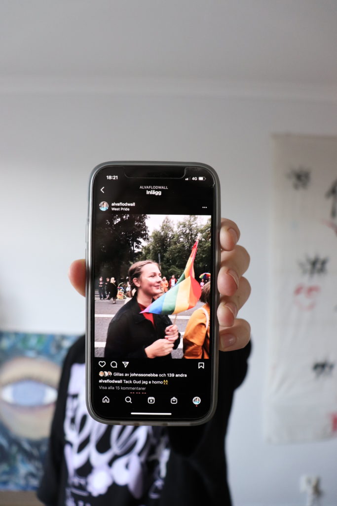 Alva Flodwall håller upp sin iPhone med en bild från hennes instragamkonto där hon håller i en prideflagga.